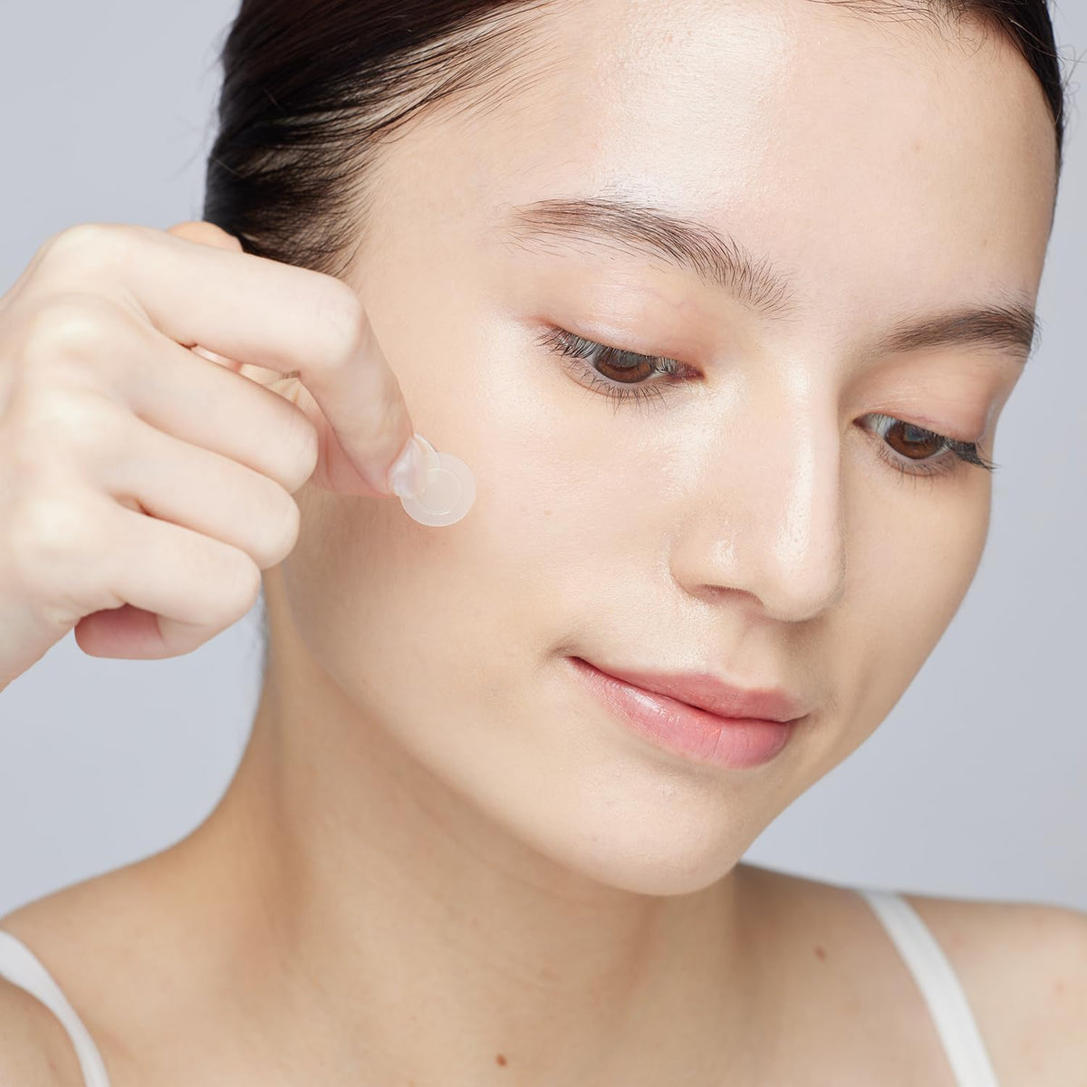 Woman applying a small clear microdart blemish patch to her cheek